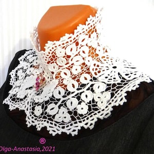 Puede incluir: Collar de encaje blanco tejido a crochet con un delicado patr&oacute;n floral. El collar se lleva sobre una camisa negra y tiene un peque&ntilde;o broche de flor rosa.