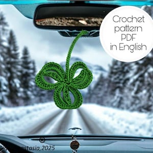 May include: A green crocheted four-leaf clover hanging from a car's rearview mirror. The text "Crochet pattern PDF in English" is visible in the upper right corner of the image.