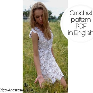 Op de afbeelding: Een vrouw in een witte gehaakte jurk staat in een veld met hoog gras. De afbeelding bevat de tekst "Crochet pattern PDF in English".