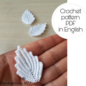 Puede incluir: Patrón de hoja de crochet blanco en formato PDF, disponible en inglés. La imagen muestra una mano sosteniendo una hoja de crochet, con otras dos hojas en el fondo.