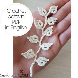 Op de afbeelding: Een crèmekleurig haakbladpatroon. Het delicate ontwerp heeft een centrale stengel met meerdere bladeren. De afbeelding bevat de tekst "Crochet pattern PDF in English" en de copyrightinformatie "Olga-Anastasia, 2022".