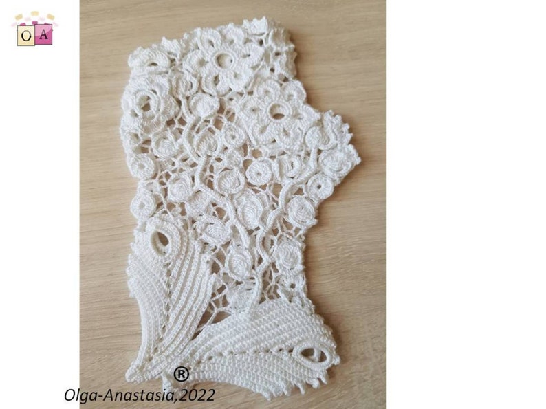 Peut inclure: Dentelle crochet&eacute;e blanche avec un motif floral. La dentelle a un bord festonn&eacute; et un motif d&eacute;licat. La dentelle est sur une surface en bois. Olga-Anastasia, 2022.