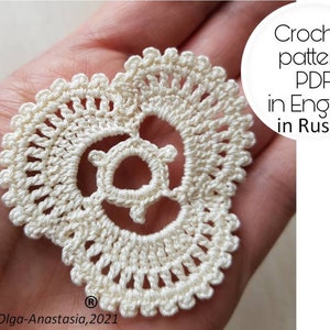 May include: A cream-colored, heart-shaped crochet doily with a detailed, openwork design. The doily features a central circular motif and a scalloped edge. Text on the image reads "Crochet pattern PDF in English in Russian".