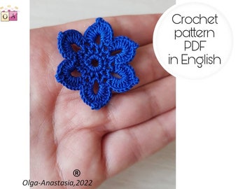 May include: A close-up of a blue crocheted flower. The flower is held in a hand. The text "Crochet pattern PDF in English" is visible in the background.