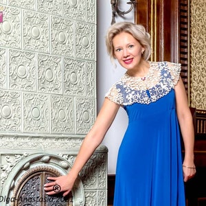 Peut inclure: Une femme portant une robe bleue avec un col en dentelle blanche se tient devant un po&ecirc;le &agrave; carrelage d&eacute;coratif.