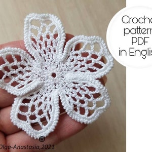 Puede incluir: Una flor blanca de ganchillo con cinco pétalos. La flor tiene un diseño calado delicado y un borde texturizado. La imagen incluye el texto "Crochet pattern PDF in English".