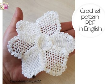 May include: White crochet flower pattern in PDF format, available in English. The pattern is shown in a hand holding the finished crochet piece.