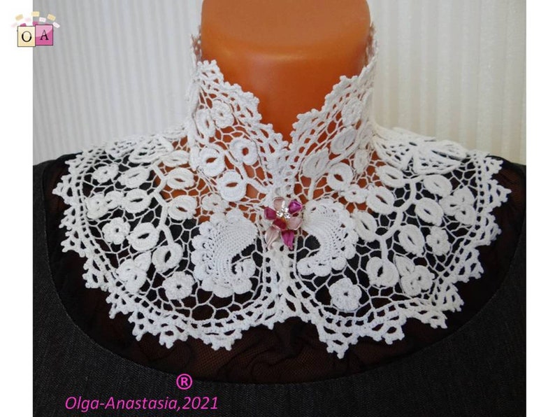 Puede incluir: Collar de encaje blanco tejido a crochet con un delicado patr&oacute;n floral. El collar tiene un escote alto y est&aacute; adornado con un broche de flor rosa.