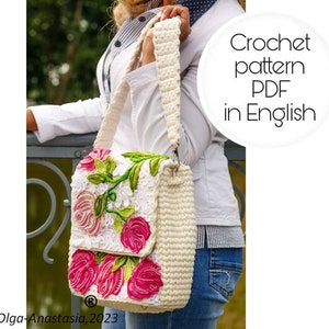 Puede incluir: Un bolso blanco de crochet con un diseño floral con rosas rosas y verdes. El bolso tiene una correa larga y se lleva al hombro. El texto "Crochet pattern PDF in English" es visible en la imagen.