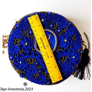 K&ouml;nnte beinhalten: Eine runde, blaue und goldene Clutch aus H&auml;kelarbeit mit einem schwarzen Quastenanh&auml;nger. Die Tasche ist mit Strasssteinen verziert und hat einen goldenen Kettenriemen.