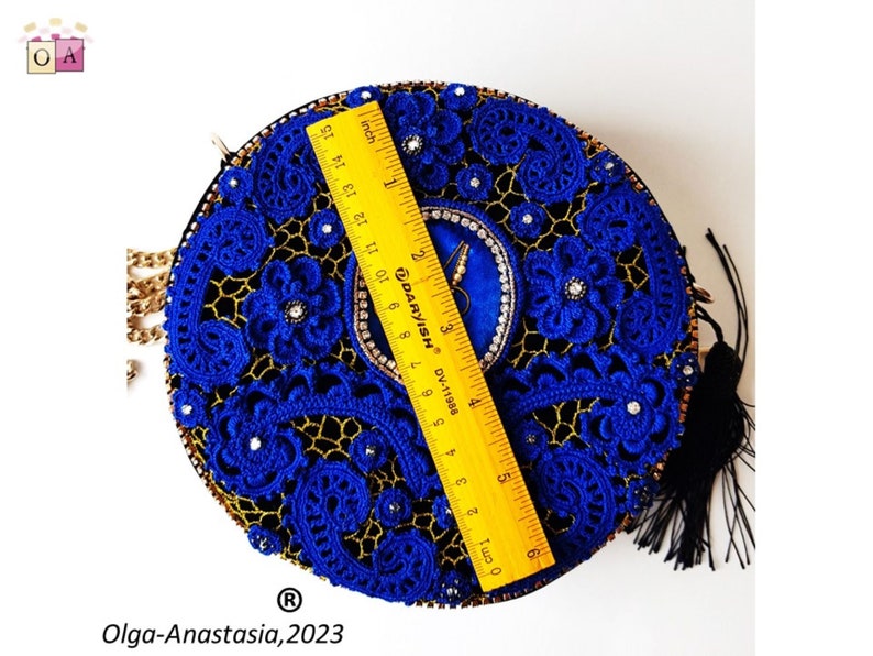 K&ouml;nnte beinhalten: Eine runde, blaue und goldene Clutch aus H&auml;kelarbeit mit einem schwarzen Quastenanh&auml;nger. Die Tasche ist mit Strasssteinen verziert und hat einen goldenen Kettenriemen.