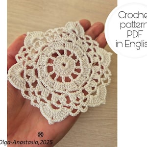 May include: A cream-colored, crocheted doily with a floral design. The doily is held in a hand and features a central spiral pattern surrounded by openwork and scalloped edges. Text on the image reads "Crochet pattern PDF in English."