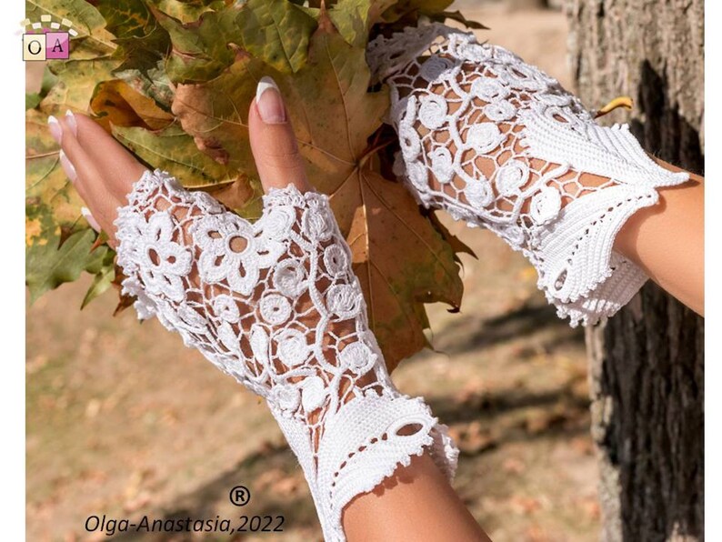 Peut inclure: Gants sans doigts en crochet blanc avec un motif floral d&eacute;licat. Les gants sont pr&eacute;sent&eacute;s sur une main sur fond de feuilles d'automne.