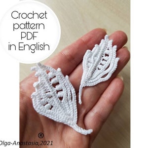 May include: Two white crocheted leaf shapes, with intricate details, are held in a hand. The image includes the text "Crochet pattern PDF in English" and "Olga-Anastasija, 2021".