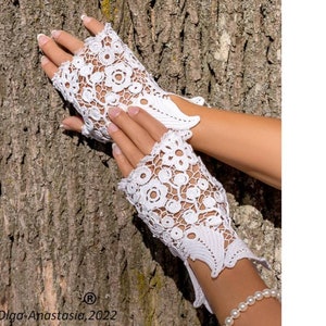 Peut inclure: Gants sans doigts en crochet blanc avec un motif floral. Les gants sont pr&eacute;sent&eacute;s sur une main sur un fond d'&eacute;corce d'arbre.
