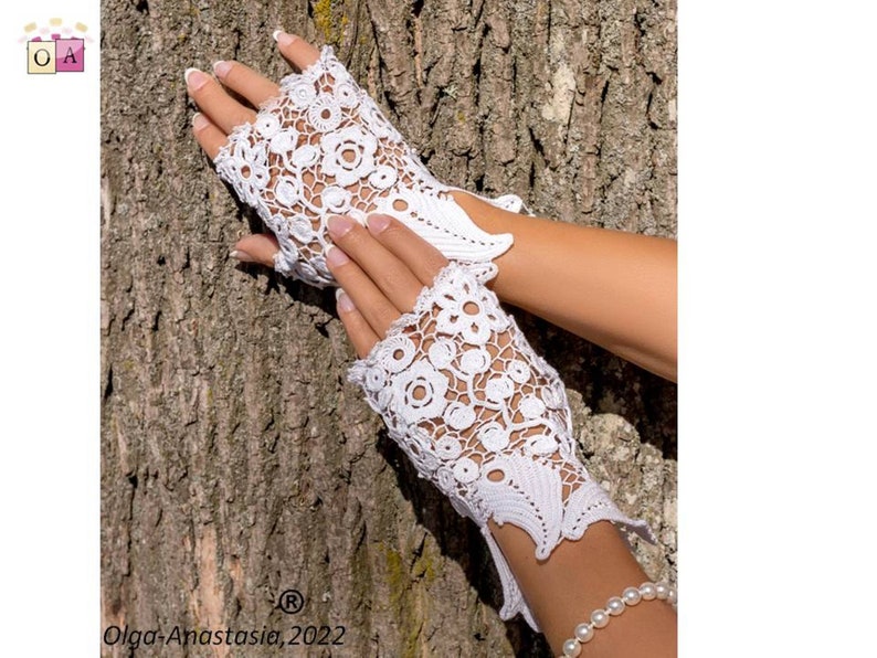 Peut inclure: Gants sans doigts en crochet blanc avec un motif floral. Les gants sont pr&eacute;sent&eacute;s sur une main sur un fond d'&eacute;corce d'arbre.