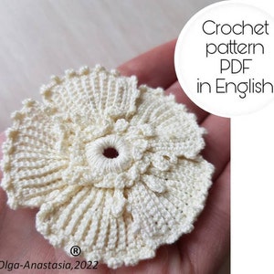 May include: A crocheted white flower with a small red centre. The flower is in the palm of a hand. The text "Crochet pattern PDF in English" is in a white circle on the right side of the image.