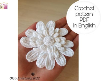 May include: A white crocheted flower with a detailed center. The flower is held in a hand. The text "Crochet pattern PDF in English" is visible in the image.