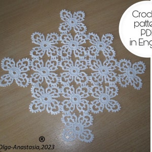 May include: White crochet doily with a floral design. The doily is made up of many small flowers, each with five petals. The doily is laid out on a wooden surface. Crochet pattern PDF in English.