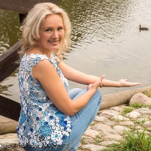May include: A woman wearing a blue and white crocheted top with a floral design, sitting on a wooden bridge by a pond with ducks. The text "Olga-Anastasia, 2021" is visible in the bottom left corner of the image.