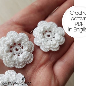 May include: Two white crocheted flowers with a detailed center. Crochet pattern PDF in English.