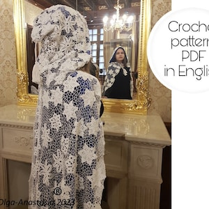 May include: A white, open-weave crochet cape with a floral pattern. The cape is draped over a person, with a matching hood. The image includes the text "Crochet pattern PDF in English". The cape is displayed in front of a gold-framed mirror.