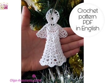 Op de afbeelding: Witte gehaakte engel-versiering, een handgemaakte kerstversiering. De engel wordt in een hand gehouden tegen een groene kerstboom achtergrond. De tekst "Crochet pattern PDF in English" is zichtbaar in een witte cirkel.