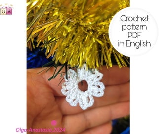 May include: A close-up of a white crocheted snowflake ornament. The ornament is held in a hand against a background of gold and blue tinsel.