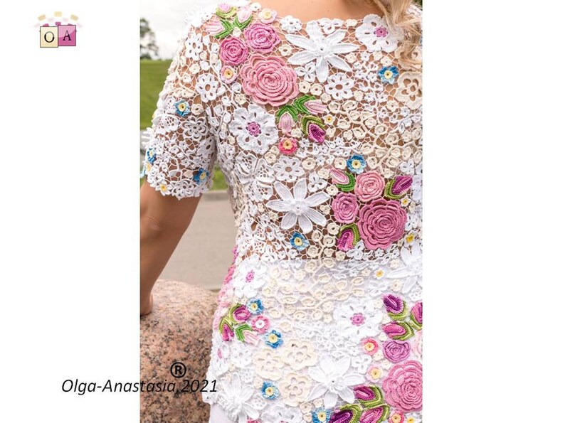 Puede incluir: Top blanco de crochet con un dise&ntilde;o floral con flores rosas, blancas y azules. El top est&aacute; hecho de encaje delicado y tiene un corte holgado y fluido.