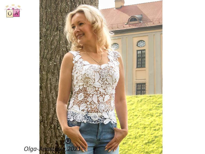 May include: A white crocheted top with a floral design. The top is sleeveless and has a scoop neck. The model is wearing blue jeans.