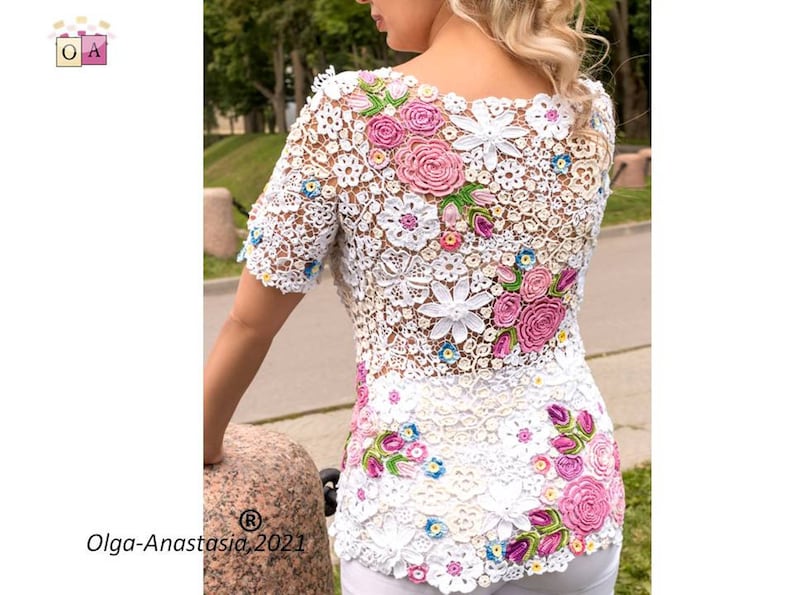 Puede incluir: Top blanco de crochet con un dise&ntilde;o floral con flores rosas, blancas y verdes. El top tiene un escote redondo y mangas cortas.