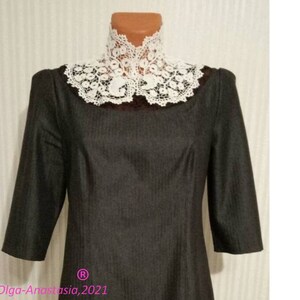 Puede incluir: Un vestido negro con un cuello de ganchillo blanco. El vestido tiene un corpi&ntilde;o ajustado y una falda ligeramente acampanada. El cuello es alto, de estilo de pie, con un delicado patr&oacute;n de encaje.