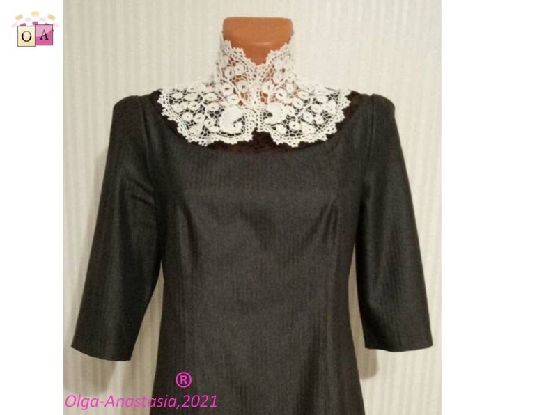 Puede incluir: Un vestido negro con un cuello de ganchillo blanco. El vestido tiene un corpi&ntilde;o ajustado y una falda ligeramente acampanada. El cuello es alto, de estilo de pie, con un delicado patr&oacute;n de encaje.