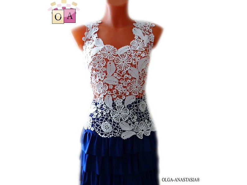 May include: White crochet top with a floral design. The top is sleeveless and has a scoop neck. The top is worn over a blue skirt.