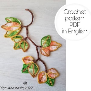 May include: A crocheted leaf branch with green, orange, and yellow leaves. The leaves are attached to a brown stem. The text "Crochet pattern PDF in English" is in a white circle. The copyright information "Olga-Anastasia, 2022" is at the bottom.