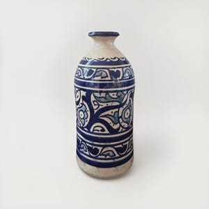 May include: A white ceramic vase with blue and green floral designs. The vase has a rounded body and a narrow neck.