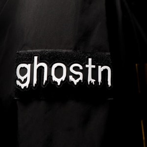 以下が含まれることがあります： 黒いジャケットに、白い「ghostn」のパッチが前面に付いています。パッチは、垂れ下がったような効果があります。