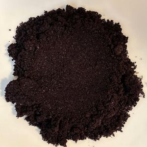 May include: A pile of dark brown, finely ground coffee, with a slightly textured appearance. The coffee grounds are densely packed, creating a rich, earthy visual. The image is taken against a plain white background.