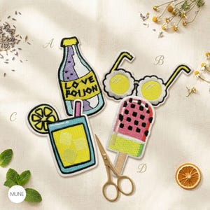 May include: Embroidered patches with summer designs. Includes a bottle with "Love Potion" text, flower sunglasses, a cocktail with lemon, and a watermelon ice lolly. Gold scissors are also present.