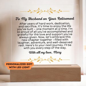 May include: A personalized acrylic plaque with a message for a husband on his retirement. The message reads "To My Husband on Your Retirement. After years of hard work, dedication, and sacrifice, it's time to enjoy the life you've built - one moment at a time. I'm so proud of all you've accomplished and grateful for the love and support you've always given. Now, let's embrace this new chapter together - filled with laughter, adventure, and well-deserved rest. Here's to your next journey. I'll be with you every step of the way. With all my love, Mary." The plaque is illuminated with LED lights and sits on a wooden base. The text "PERSONALIZED GIFT WITH LED LIGHT" is printed below the plaque.