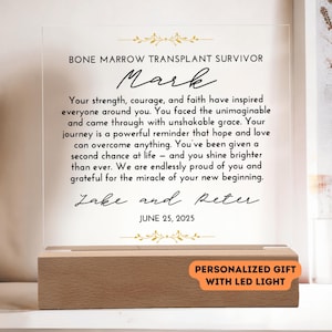 May include: A personalized acrylic gift with an LED light, featuring the text "BONE MARROW TRANSPLANT SURVIVOR Mark". The inscription includes a message of support and the names "Jake and Peter", with the date June 25, 2025.