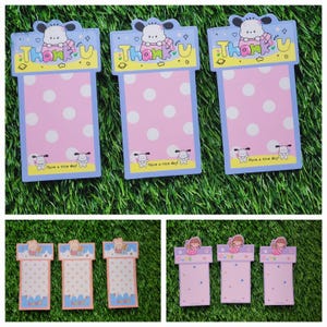 May include: Three sets of pink and blue memo pads with cartoon dog illustrations. The top of each pad has a white polka dot background with the word "Thank U" in yellow letters. The bottom of each pad has a white polka dot background with the text "Have a nice day!" in black letters.