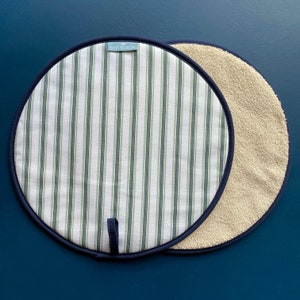 May include: A pair of round pot holders. One side is white with green stripes and a navy blue trim. The other side is a beige terry cloth with a navy blue trim. The pot holder with the stripes has a navy blue loop handle. The label on the striped pot holder reads "WILLIS BLOOM".