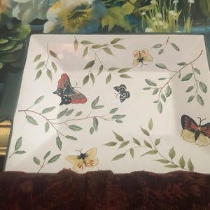 May include: Square, white ceramic serving dish with green trim and handles. The dish is decorated with painted butterflies in various colors and sizes, along with green leafy branches.