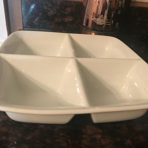 May include: White ceramic serving dish with four divided sections. The dish is designed for serving snacks, dips, or appetisers.