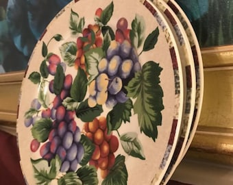 May include: A stack of three beige ceramic plates with a grape cluster design. The plates feature a border with a maroon and white checkered pattern. The grape clusters are in shades of purple, red, and orange, with green leaves.