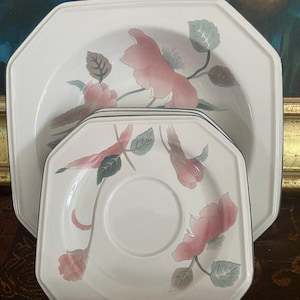 May include: A set of white octagonal dinnerware featuring a floral design with pink and gray flowers and green leaves. The set includes a large serving dish and a smaller plate with a cup indentation.