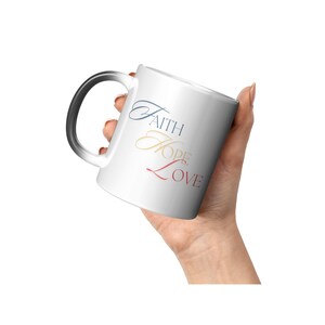 May include: White ceramic coffee mug with a black handle. The mug has the words "Faith Hope Love" written on it in a cursive font. The words are in different colors: blue, yellow, and red.