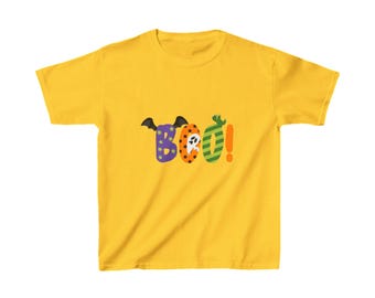 May include: Yellow short-sleeved t-shirt featuring the word "Boo!" in colourful, patterned letters. The "B" has a bat wing design, the "o" has a ghost, and the exclamation mark is green and orange striped. A fun Halloween-themed tee.