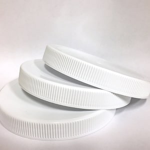 May include: Three white plastic lids with a ridged edge. The lids are stacked on top of each other.